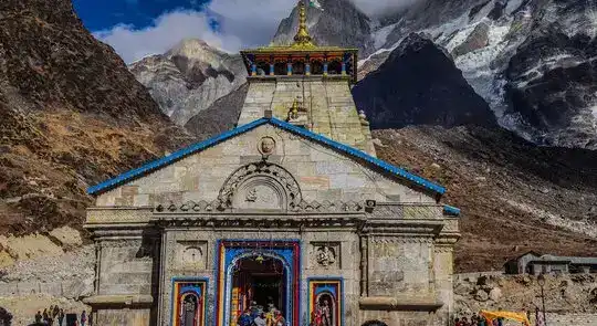 Kedarnath Temple, a stone structure with a blue roof, nestled amidst snow-capped Himalayan mountains.